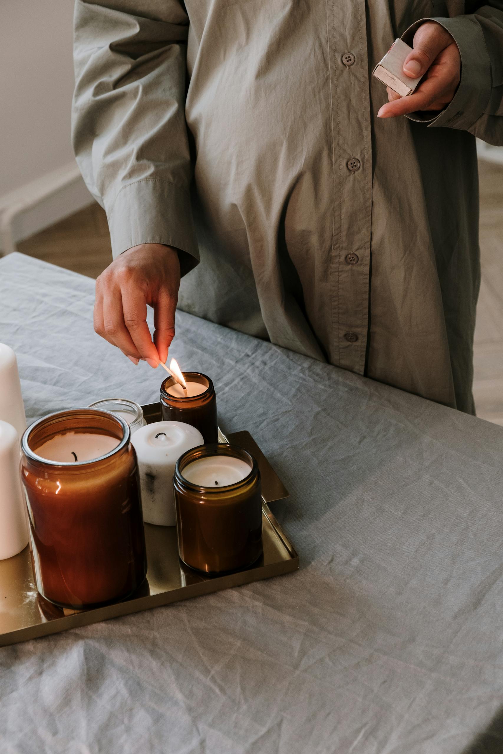 A pregnant woman gently lights candles on a tray, creating a warm and peaceful atmosphere indoors.
